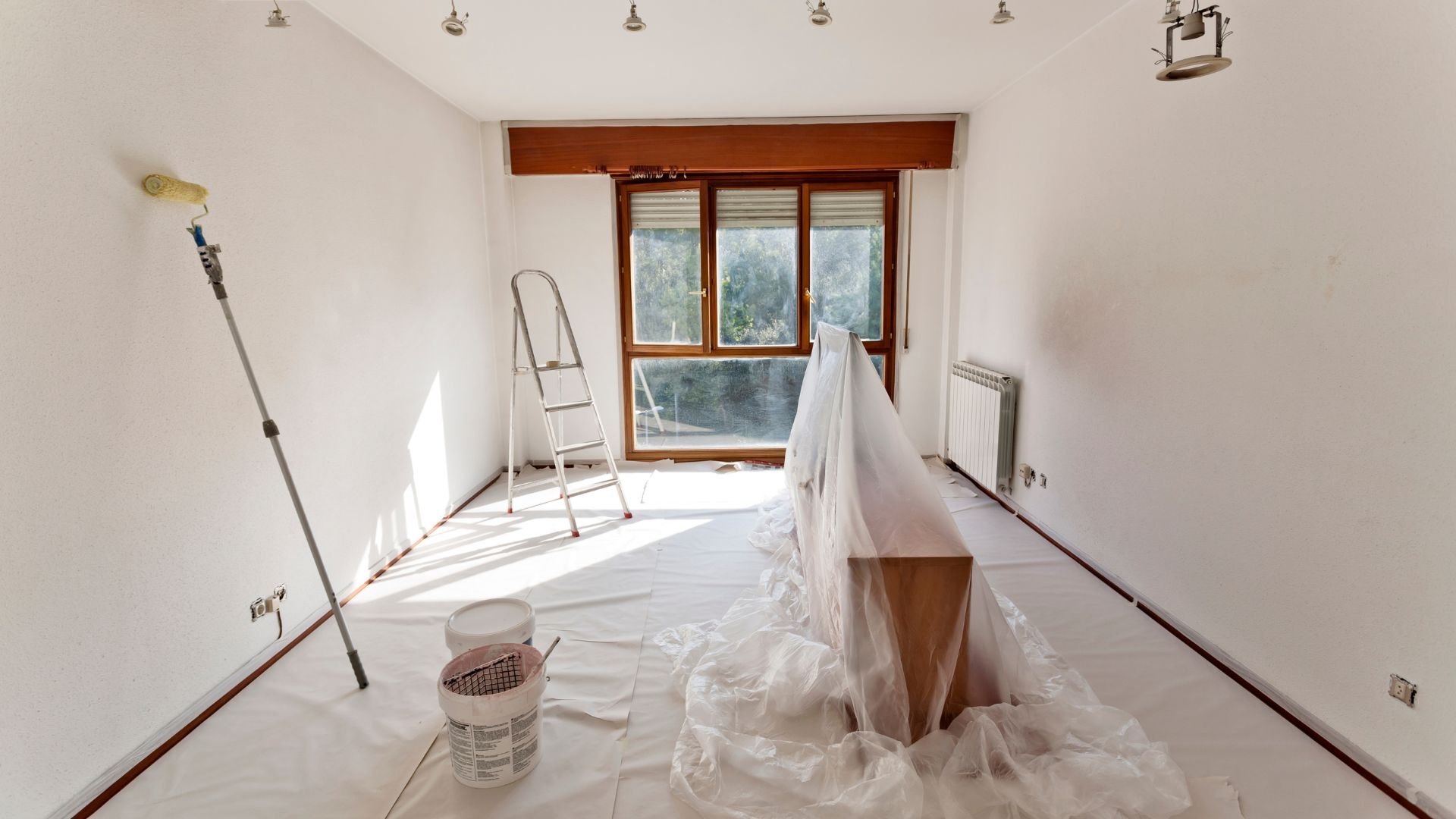 Room interior during painting with ladder, drop cloths, and paint supplies