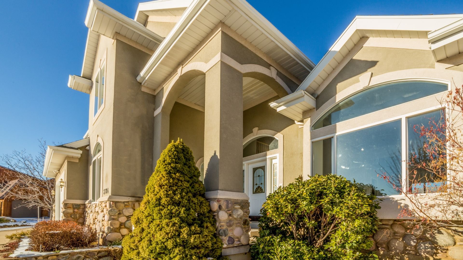 Large two-story house with stone accents and green landscaping on sunny day