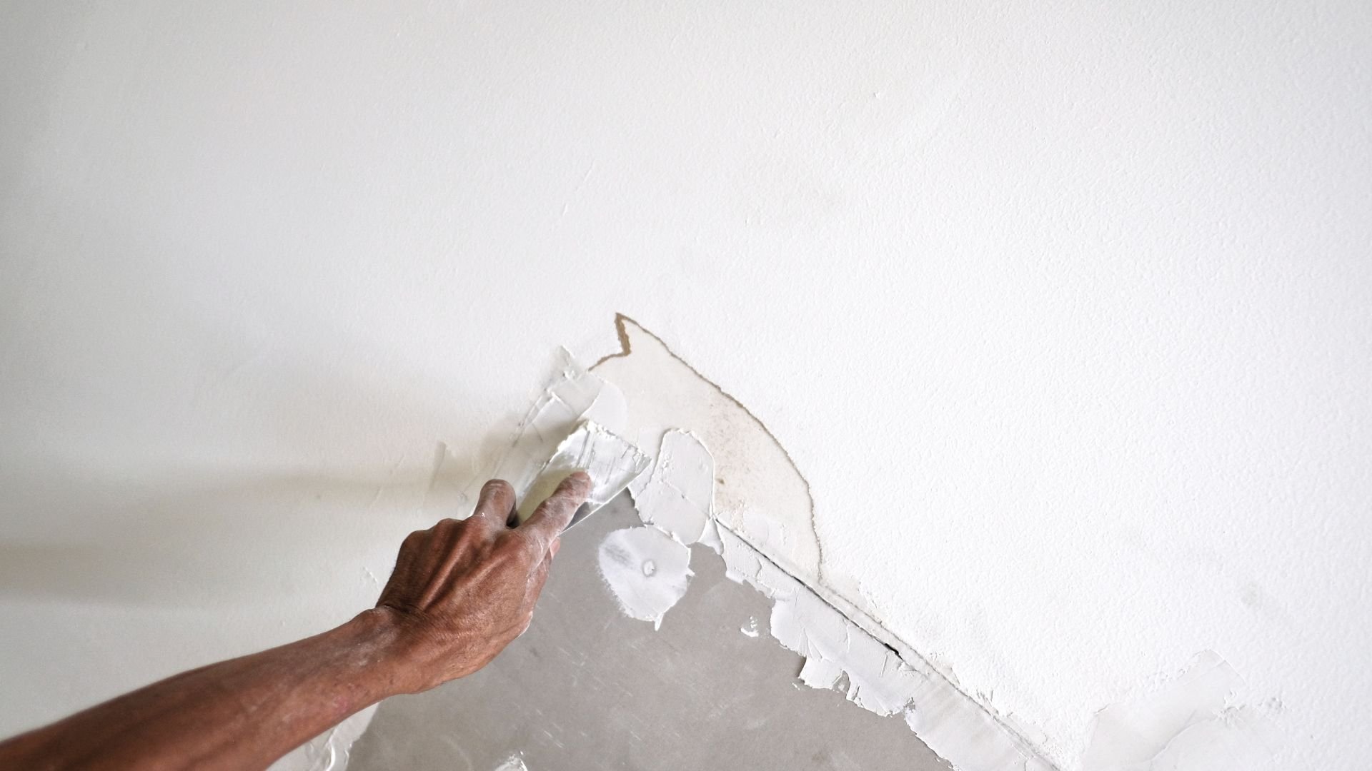 Hand peeling off white wallpaper or paint from wall surface