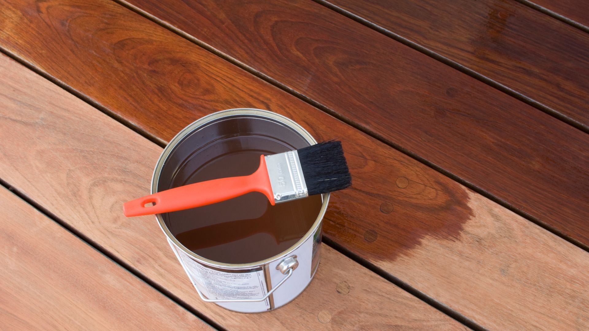 Red paintbrush resting on an open brown wood stain can