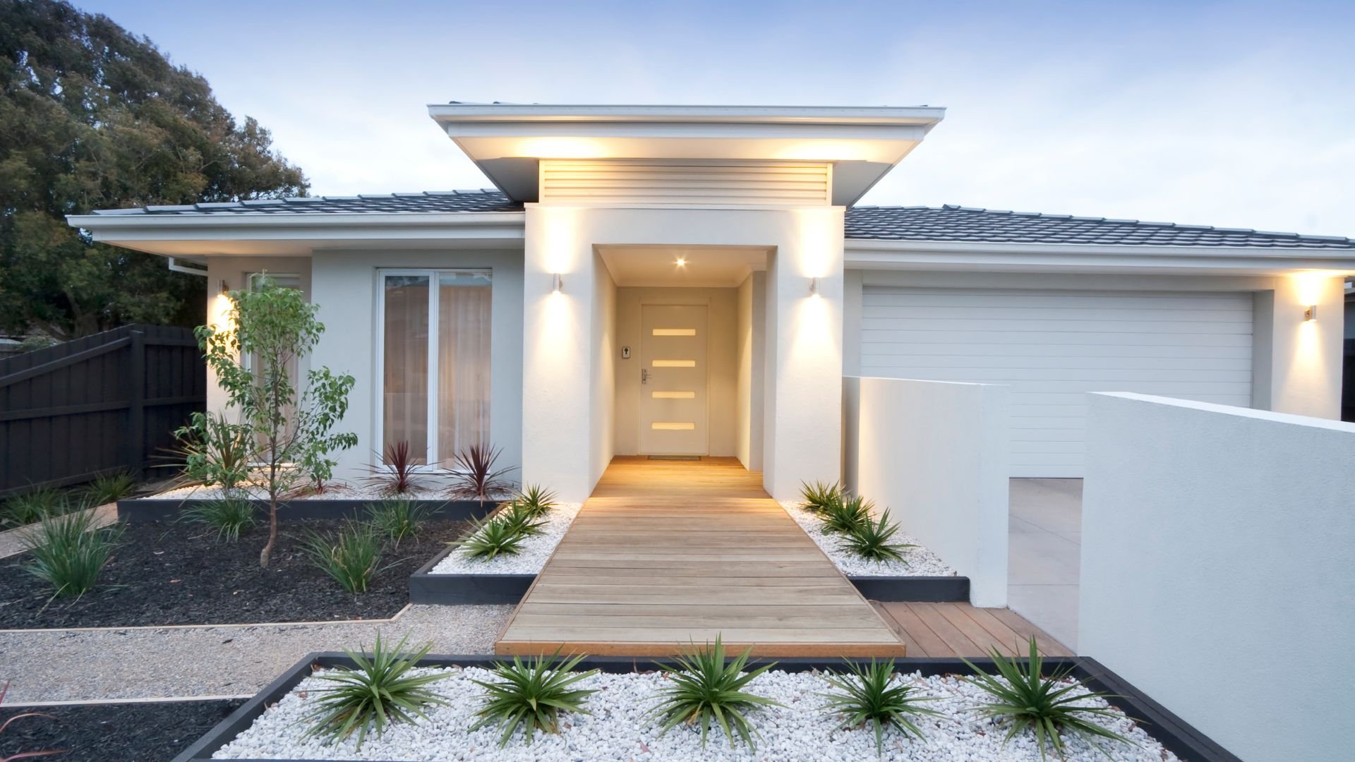 Modern white house with wooden walkway and minimalist landscaping at dusk