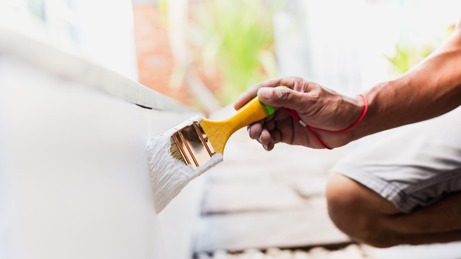 Hand painting wall with white paint using a yellow-handled brush