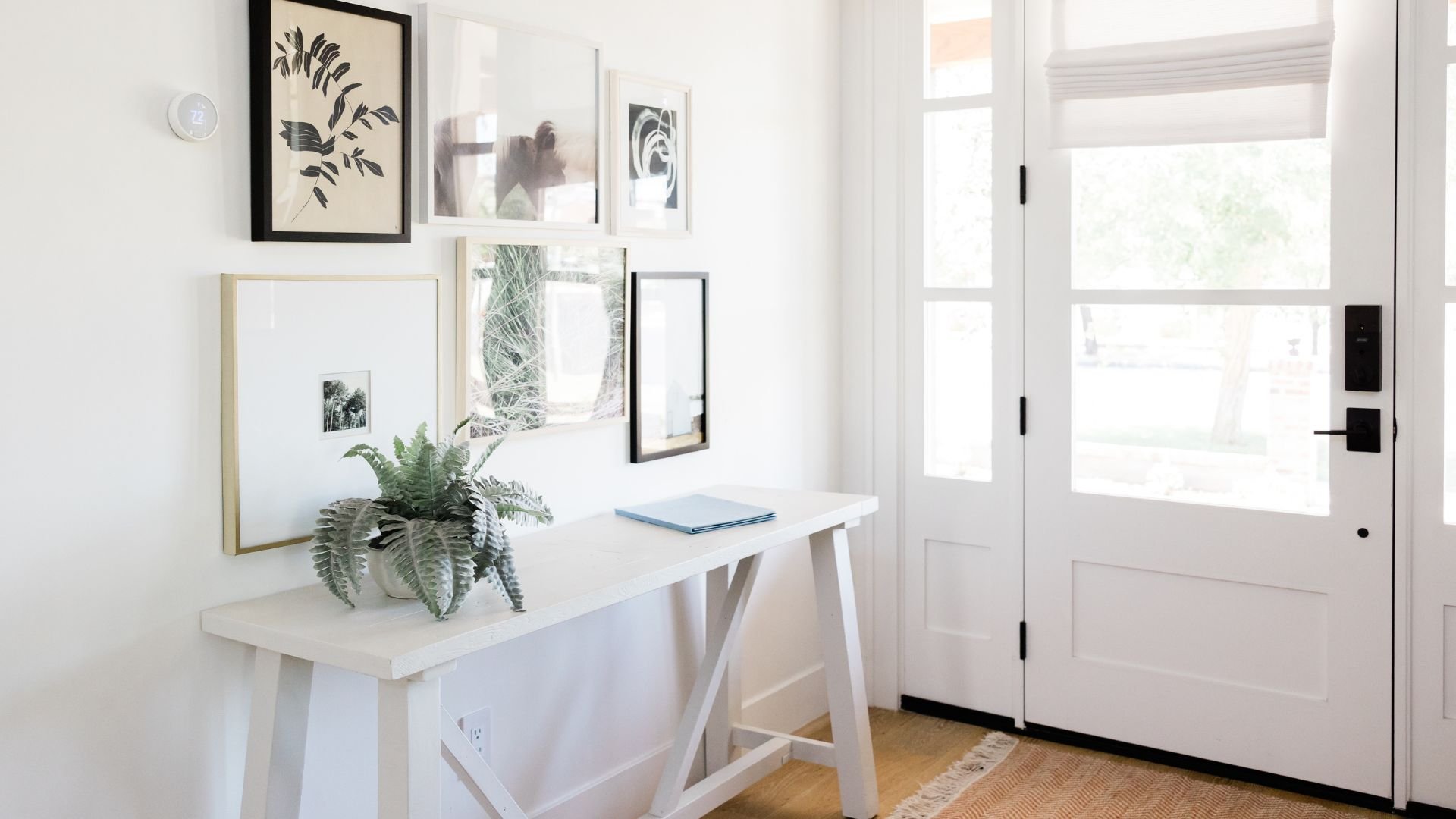 Minimalist entryway with white table, fern, gallery wall, and glass door