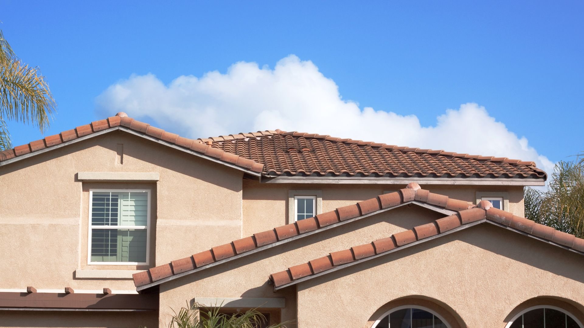 Stucco house with terracotta roof tiles against blue sky with clouds