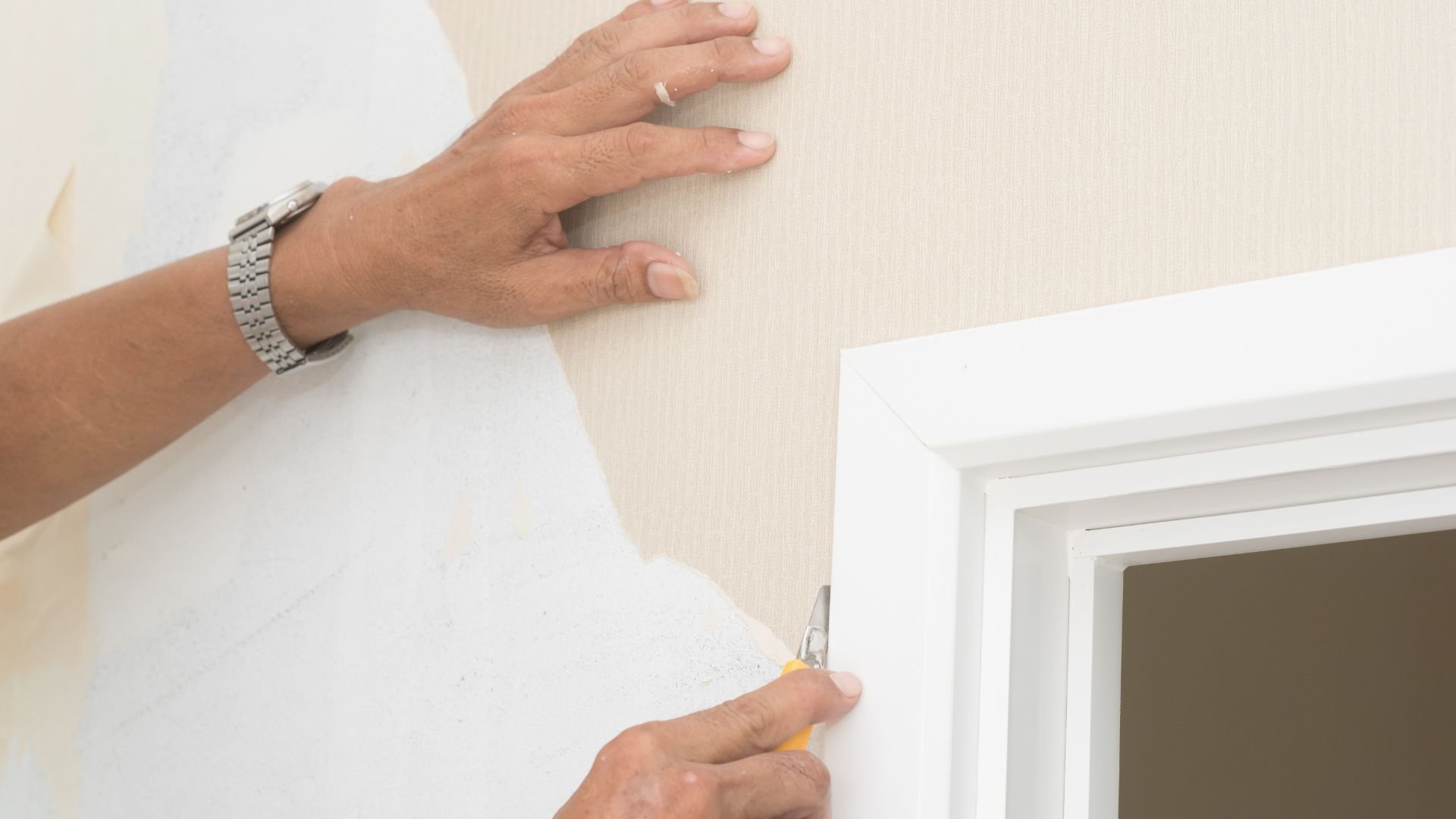 Hands installing wallpaper near a white-framed window or doorway