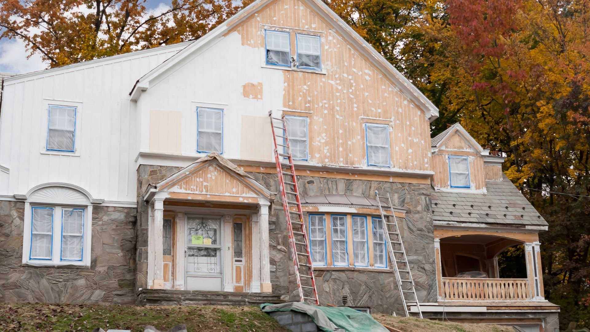 Large house with stone base undergoing exterior painting during autumn