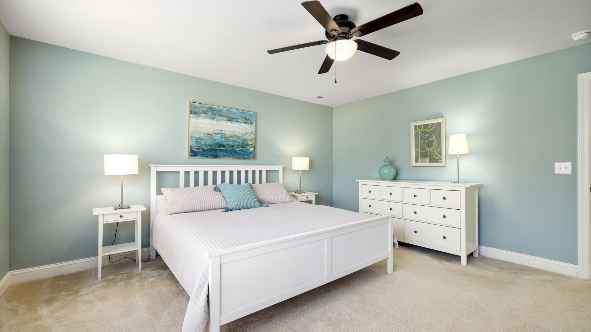 Serene bedroom with white furniture, blue walls, and coastal artwork